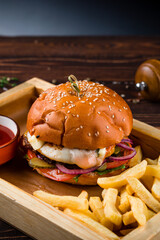 Wall Mural - American beef burger with tomato, fried eggs, pickle, onion, lettuce, cheese sauce on a wooden board with french fries and ketchup.