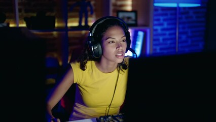 Poster - Young african american woman streamer playing video game using computer at gaming room