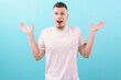 © AndriiKoval - A сaucasian happy and surprised man in a white t-shirt looks at the camera spreading his hands to say wow on blue background. Outfit. Shocked. Modern. Style. Arm. Expression. Lifestyle. Overwhelmed