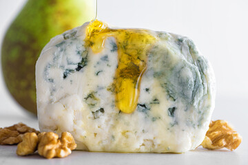 Wall Mural - Pouring honey on blue cheese dorblu or gorgonzola with pear and walnuts on white background. Close up