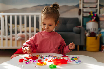 A little girl playing with red heart from play dough for modeling and  decorations from crystal rhinestones and shiny stones. Toddlers crafts for Valentine's Day. Holiday Art Activity for Kids.