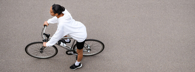 Wall Mural - Overhead view of fit african american woman in hoodie cycling on road on street, banner shot 