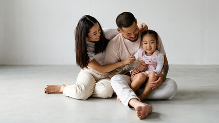 Wall Mural - Banner image of smiling barefoot asian parents and toddler child sitting on grey background