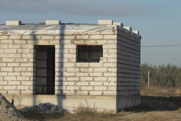 Canvas Print - part of one white brick unfinished house on the street in the grass against the blue sky