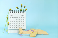 Selective Focus Of March 2023 Desk Calendar With Wooden Airplane Model And Spring Season Flowers. Spring Season Travel Holiday Concept.
