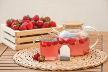 Wall Mural - Strawberry drink from a tea bag in a cup and teapot with fresh fruits on the background of a wooden crate full of red berries