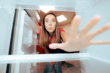 Wall Mural - Hungry Woman Reaching for Something to Eat in the Fridge. Surprised girl choosing a healthy snack from her refrigerator 
