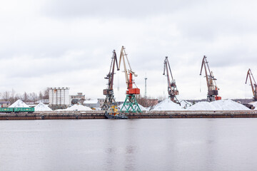Poster - River port in winter. Port cranes on the bank of the river. Embankment of the river port, a barge at the quay wall. Large port cranes on the river. Extraction and transportation of sand other cargo