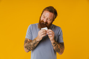 Wall Mural - Bearded happy man eating chocolate bar while standing isolated