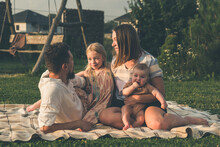 Happy Family And Small Children On A Blanket In The Grass At Summer