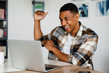 Canvas Print - Positive african man gesturing while having video call via laptop at home