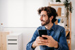 © Westend61 - Thoughtful smiling young engineer holding smart phone sitting at desk in office