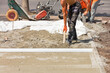 © Sergii - A team of workers with a shovel levels the sandy foundation under the aluminum level for the subsequent laying of paving slabs.