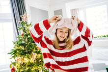 Happy Girl Wearing Rabbit Hat By Christmas Tree At Home