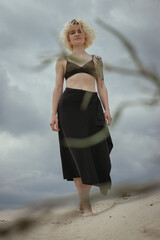 Wall Mural - Smiling woman walking along sand beach scenic photography. Picture of person with cloudy sky on background. High quality wallpaper. Photo concept for ads, travel blog, magazine, article