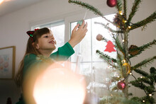 Smiling Girl Holding Bauble Hanging On Christmas Tree At Home