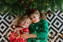Happy Sisters With Illuminated String Lights Lying Down Near Christmas Tree