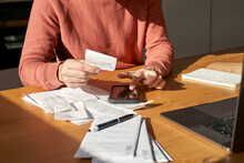 Hands Of Man With Financial Bills Calculating On Smart Phone At Desk