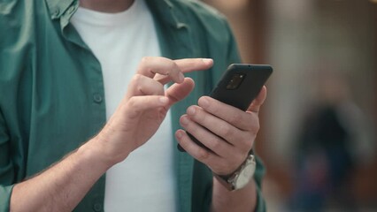 Close-up view of attractive young caucasian man's hands using smartphone online checking social media making internet payments. Focused modern adult male typing texting scrolling on phone outside.