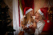 © keleny - Cute mother and daughter in the red hats of Santa Claus assistants in a room decorated for Christmas. The tradition of decorating house and dressing up for the holidays. Happy childhood and motherhood