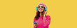Leinwandbild Motiv Portrait of happy smiling modern young woman in wireless headphones listening to music with smartphone wearing knitted sweater, pink hat on yellow background