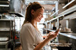 © Drobot Dean - Young blonde woman using cellphone while working in restaurant kitchen