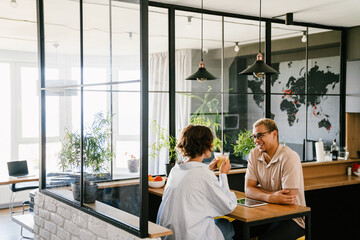 Two smiling colleagues talking during coffee break in office kitchen