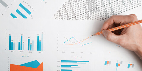 Close-up of an office worker's hand analyzing financial results, economic indicators, business reports with infographics