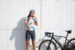 © VISTA by Westend61 - Happy cyclist adjusting helmet standing in front of white wall on sunny day