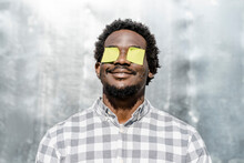 Smiling Man With Yellow Adhesive Notes On Eyes In Front Of Wall