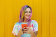 © VISTA by Westend61 - Happy young woman holding mobile phone in front of yellow wall