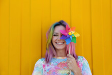 Happy Woman Wearing Tie Dye T-shirt Holding Colorful Pinwheel Toy In Front Of Yellow Wall