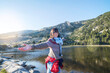 © Cavan Images - Portrait of happy woman with arms outstretched standing by lake against clear sky during sunny day