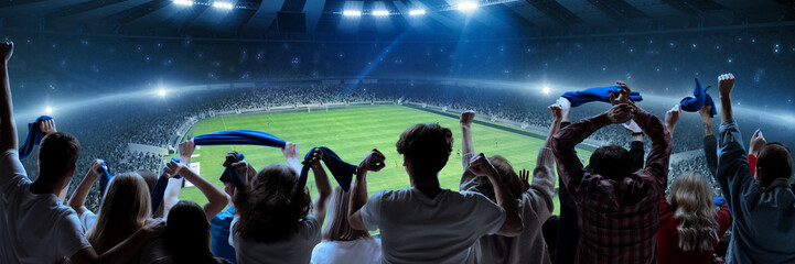 Wall Mural - Back view of football, soccer fans cheering their team, holding flag at crowded stadium at evening time. Burst of emotions. Concept of sport, hobby, leisure time, football