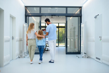 Wall Mural - Rear view of young multiracial doctor talking with mother and little girl at hospital corridor,showing them x-ray image.