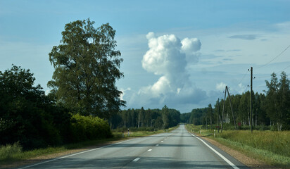 Wall Mural - A breathtaking landscape of an empty road stretching till horizon. A sunny summer day with bright blue sky, cloud and green trees. Picturesque and scenic higway in Latvia's countryside. Wanderlust