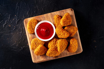 Wall Mural - Chicken nuggets with ketchup on a black background, overhead flat lay shot. A crispy meat snack at a restaurant, a fast food dish
