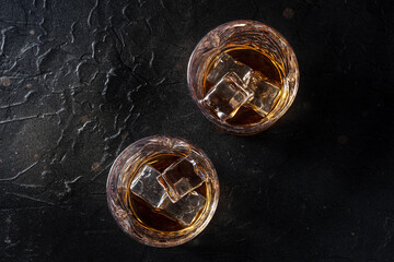 Whiskey in glasses with ice. Bourbon whisky on rocks on a black stone background, overhead flat lay shot