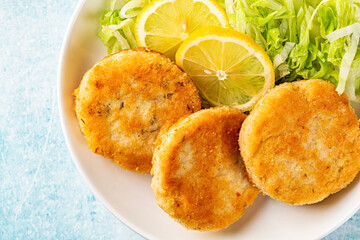 Canvas Print - Top view of Fish cakes or burger, or cutlets. Made from ground perch and tuna with herbs, breaded and fried, served with iceberg salad, lemon slices. 