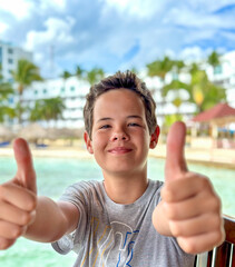 Poster - Young boy is enjoying on the beautiful tropical beach at summer showing thumbs up.