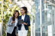 © PaeGAG - Two Asian businesswomen discussing business information while standing outside the office.