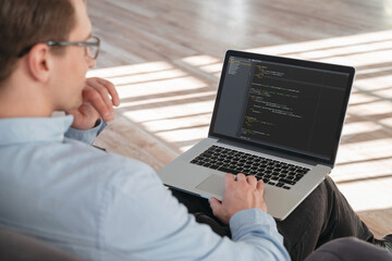 Wall Mural - close up shot of coder sitting with laptop on knees, working online on new it product.