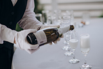 Wall Mural - waiter pouring wine into a glass with a bottle of champagne