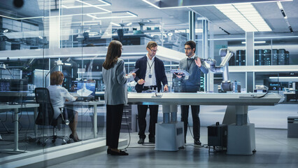 Wall Mural - Diverse Team of Industrial Robotics Engineers Gathered Around a Table With Robotic Arm. Scientists Use Tablet Computer to Manipulate and Program the Robot to Pick Up and Move a Metal Component.