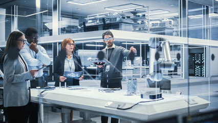 Leinwandbilder - Robotics Engineers, Project Manager and Machinery Operator Collaborate on a Robot Arm Project, Standing with Tablet Computers in Scientific Technology Lab. Team Developing an AI Robotic Arm.