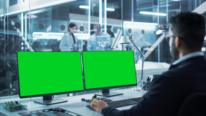 Industrial Engineer Working on a Desktop Computer with Two Green Screen Chromakey Display Screens in a Modern Technological Research and Development Center. Over the Shoulder Shot.