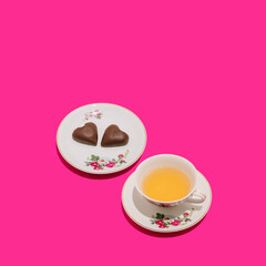 Wall Mural - Retro romantic composition of vintage cup of tea and two chocolate hearts on vivid pink background. Minimal love or Valentine's Day idea.