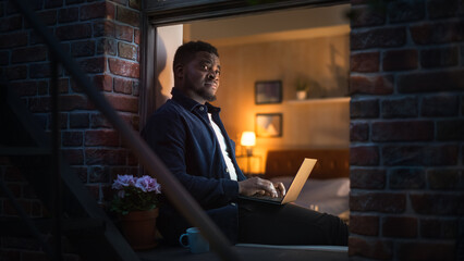 Poster - Young Handsome African American Man Working from Home on Laptop Computer in Windowsill at Night. Creative Male Checking Social Media, Browsing Internet, Investing. Urban City Lifestyle