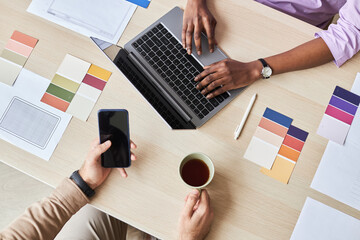 Top view closeup of two designers using laptop while working on UI project in office, flat lay with color swatches