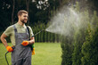 © Petro - Garden worker watering grass and bushes in the yard with sprinkler